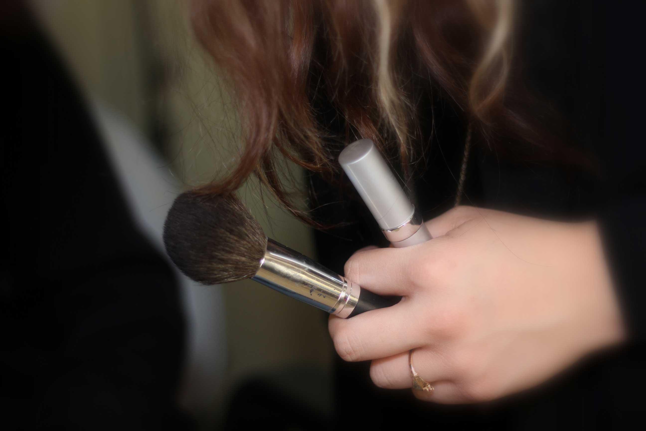 A woman holding a makeup brush and lipstick.