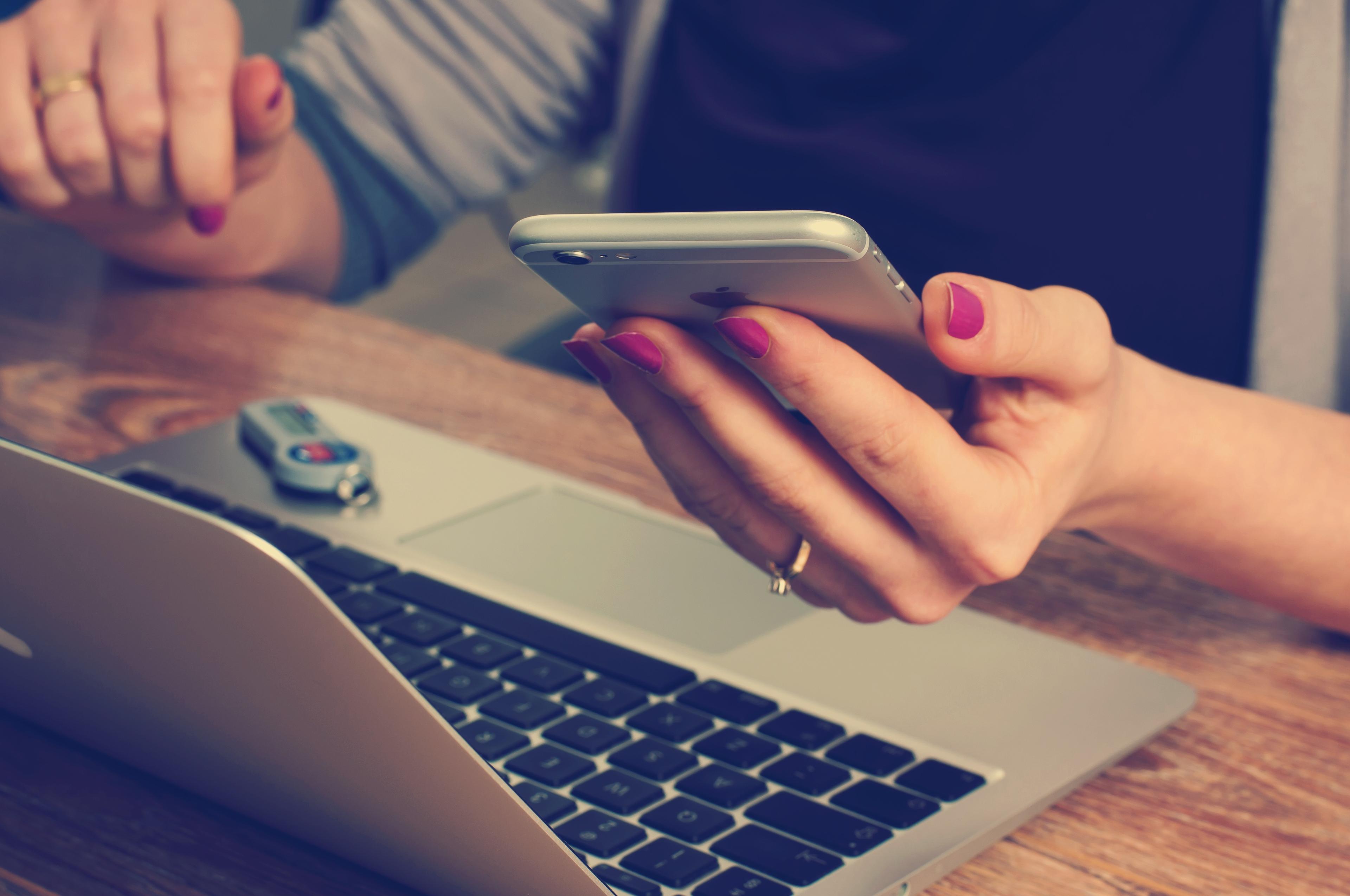An image of a person at a laptop holding a phone.