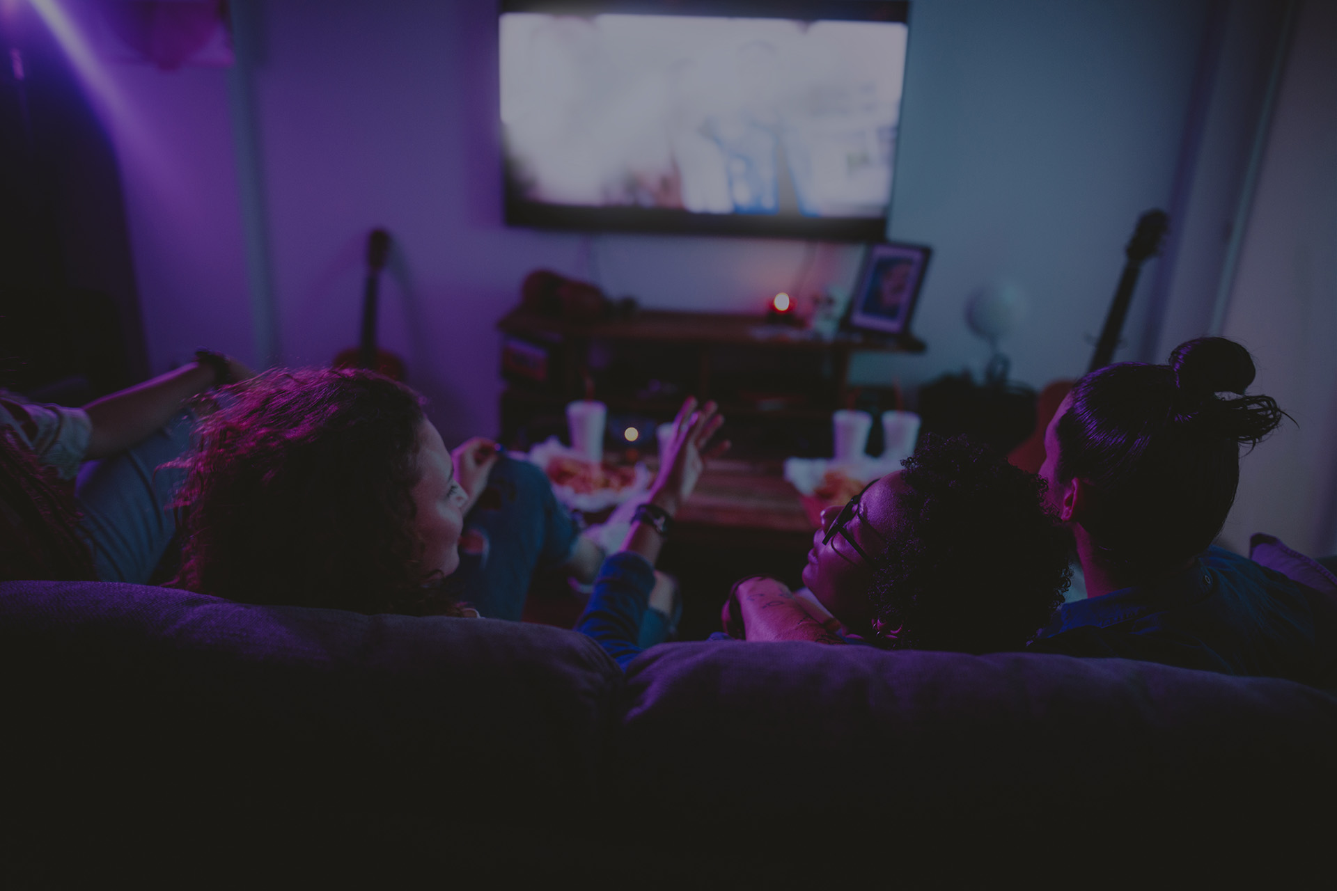 Multi-ethnic teenage friends watching TV together at hangout house.